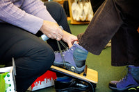 one of the owners of birkenstock village fits a guests on a fitting stool while wearing dansko clogs in santa rosa, ca 