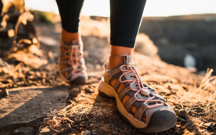 woman wearing black pants and keen astoria sandals, walking on rocks