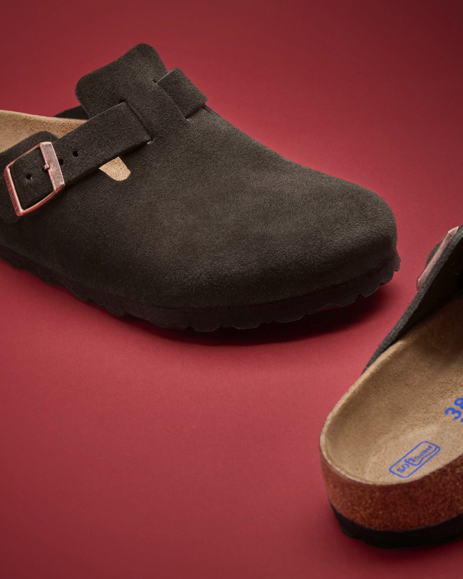 Dark green suede clog shoe with a strap on a red background